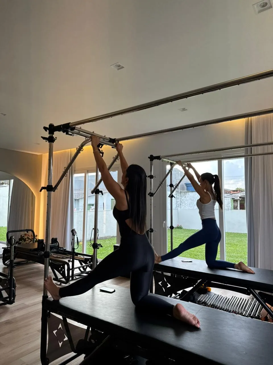 Duas alunas em exercício no cadillac, com vista para o jardim do studio